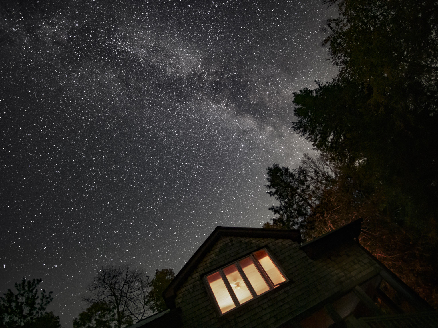 The Milky Way above a cabin with lights on